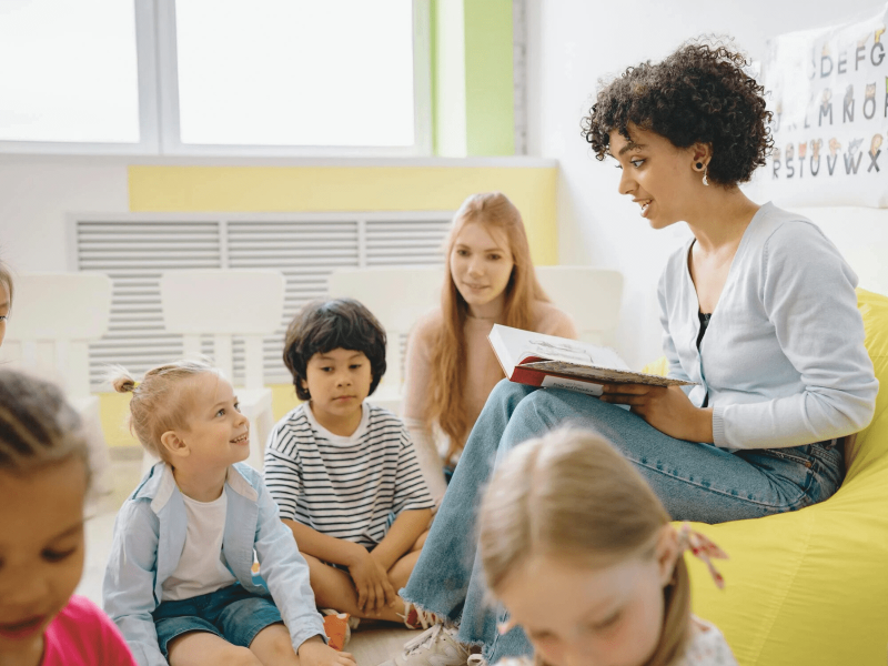 eine Grundschullehrerin liest ihren Schüler*innen ein mehrsprachiges Buch vor