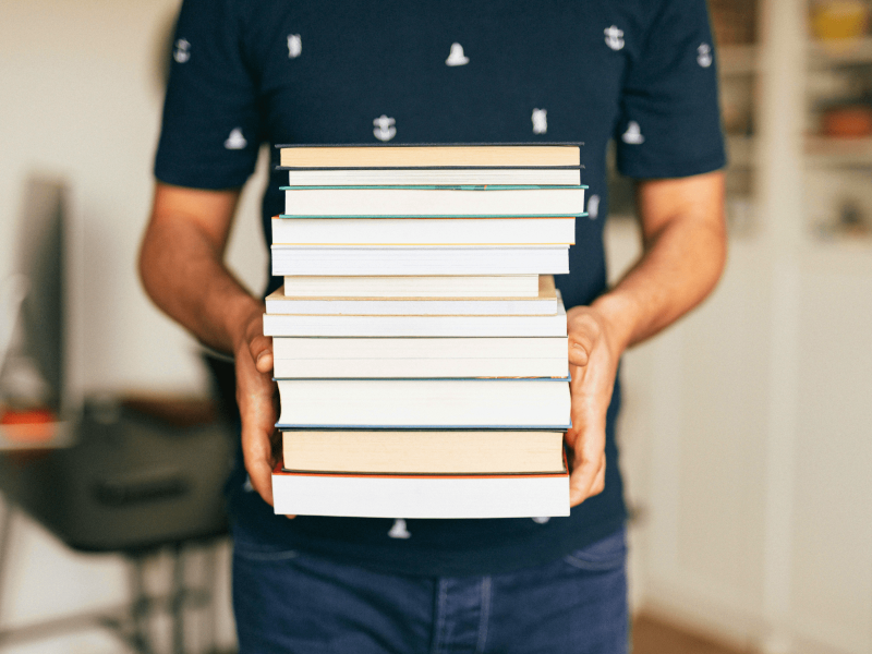 Ein Stapel von Büchern wird von einer Person getragen