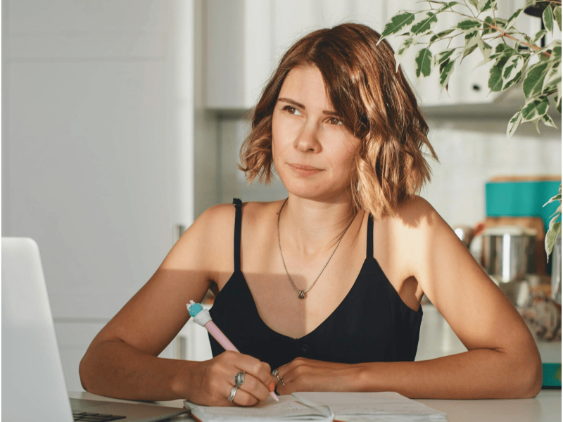 eine weiße Frau hält einen Stift in der Hand und blickt nachdenklich in die Ferne