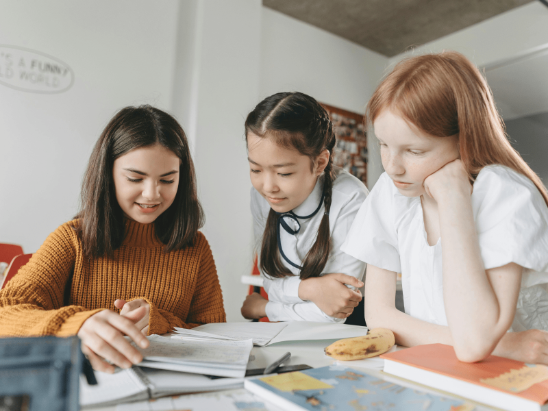 drei junge Schülerinnen beugen sich über einen Tisch und lesen gemeinsam einen DaZ-Text durch